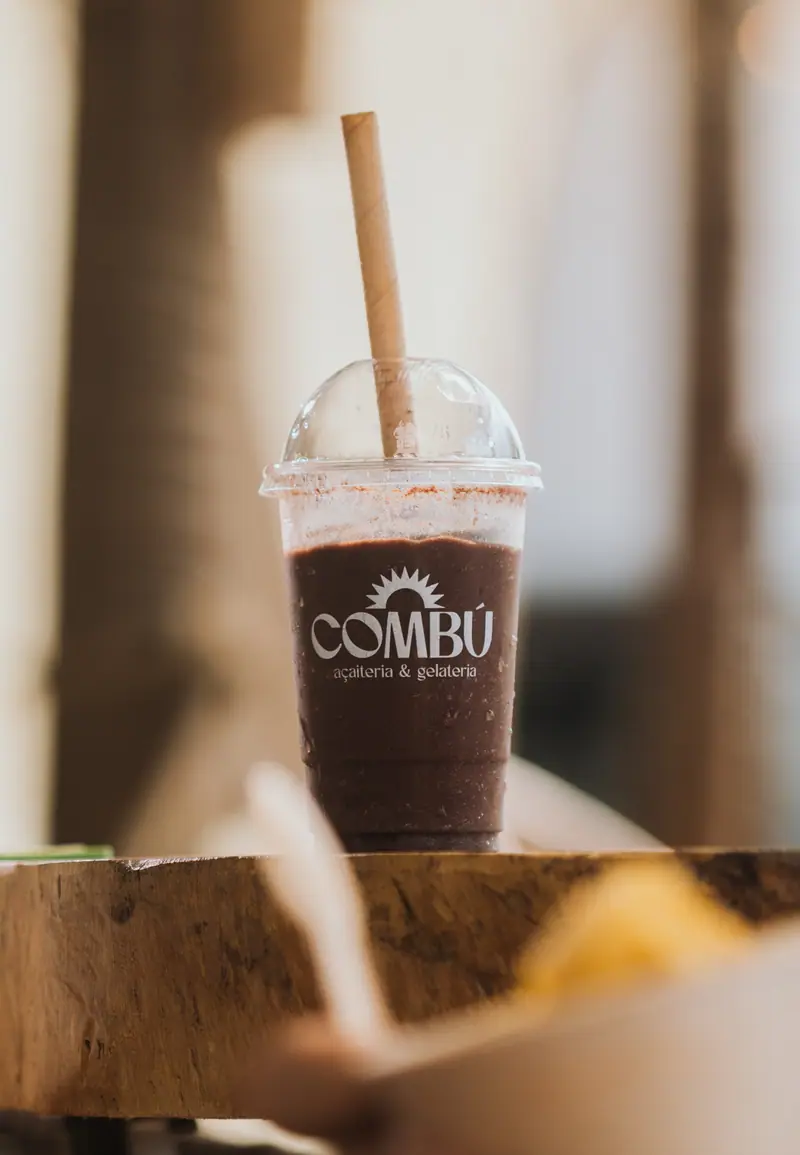 Copo de açaí batido com tampa de cúpula e canudo, sobre um toco de madeira