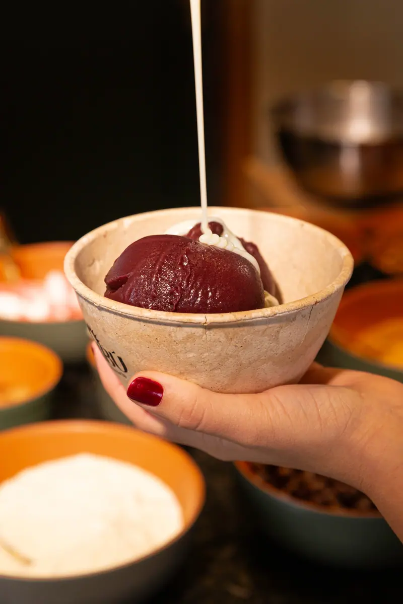 Fio de cobertura branca caindo sobre a bola de açaí no copo