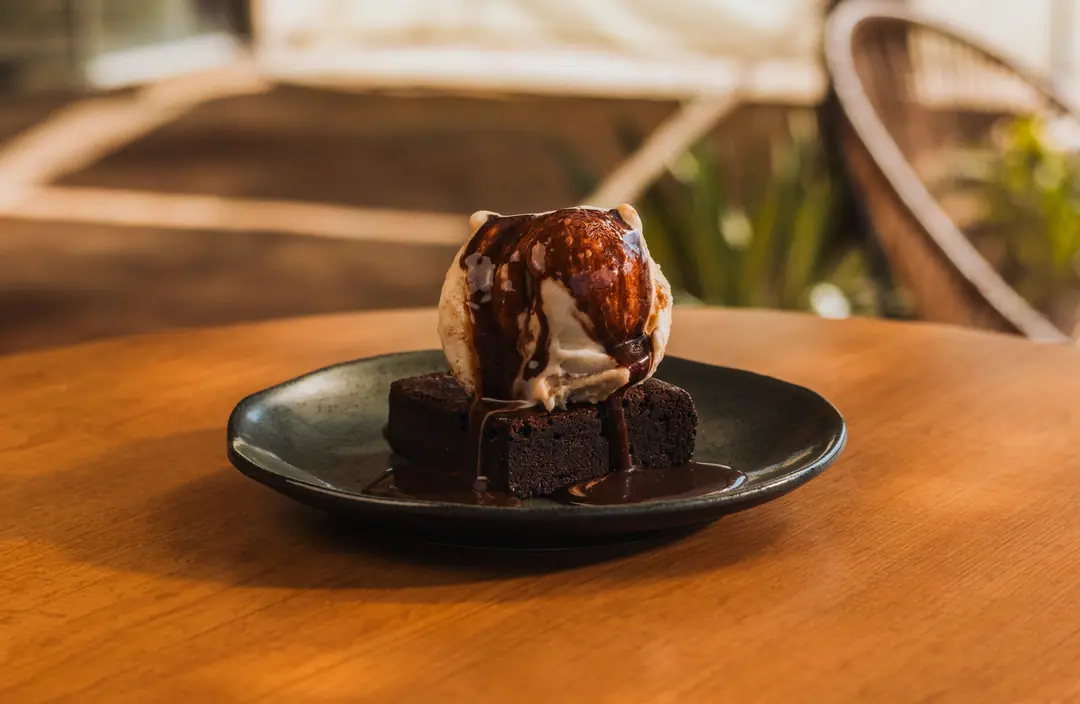 Brownie com bola de sorvete e calda num prato escuro, na mesa de madeira