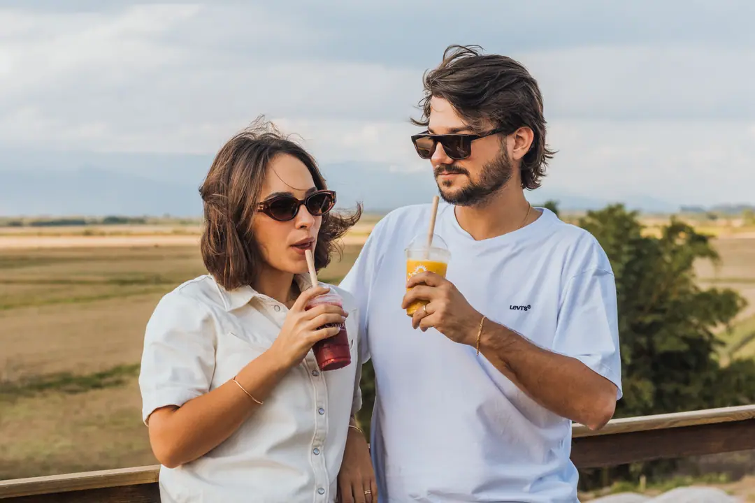 Casal brindando com as bebidas geladas da COMBÚ no mirante, com o campo ao fundo