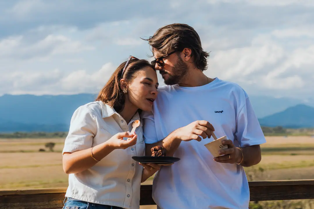 Casal rindo encostado no guarda-corpo do mirante, com a serra ao fundo
