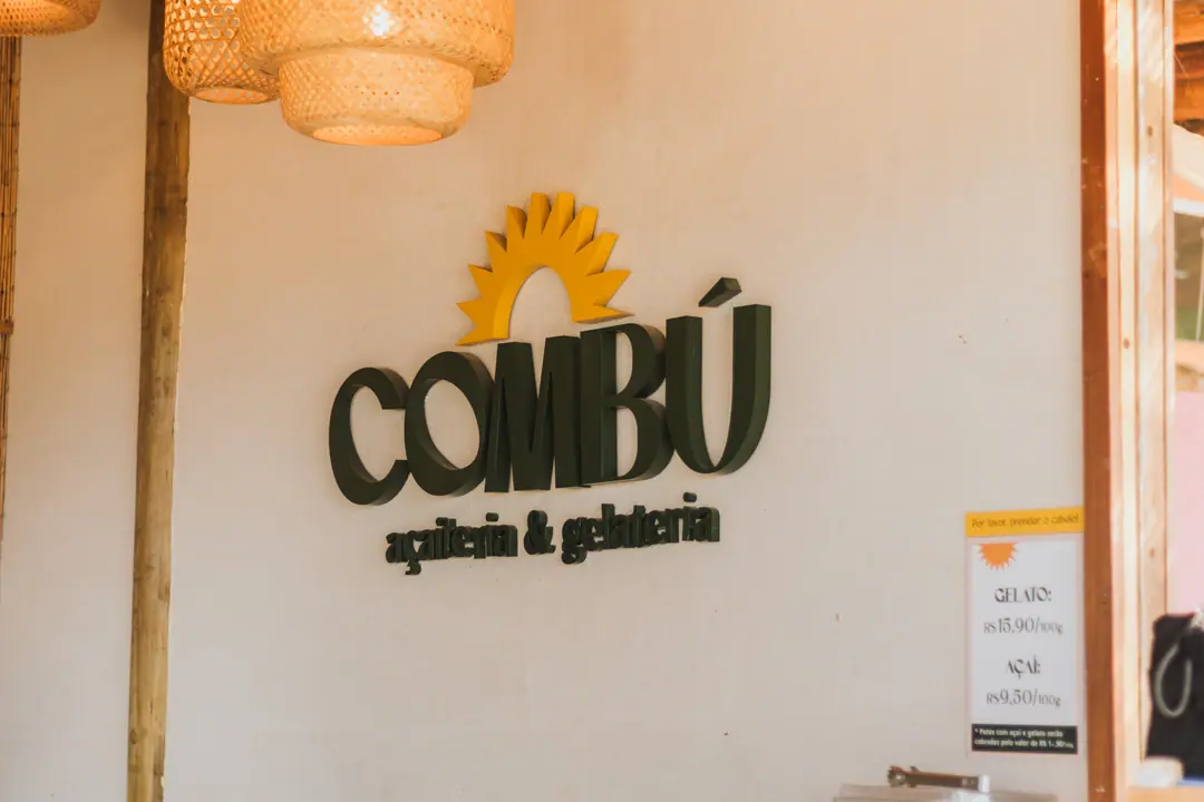 Letreiro da COMBÚ na parede do salão, com luminária de palha