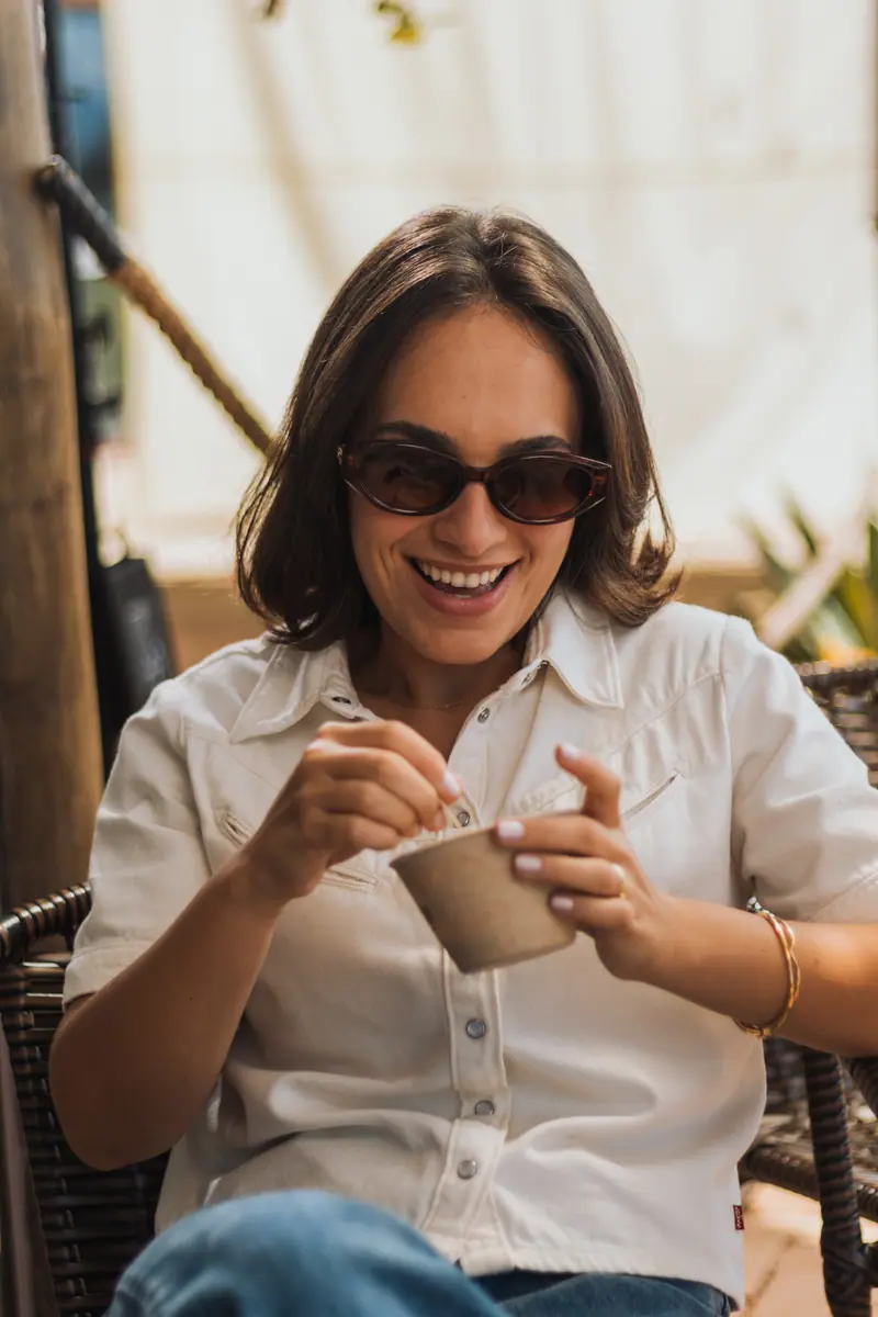 Mulher de óculos escuros sorrindo com um copo da COMBÚ nas mãos, no deck